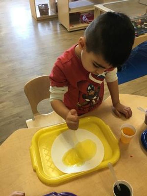 Child playing with yellow liquid on a white paper plate in a yellow tray
