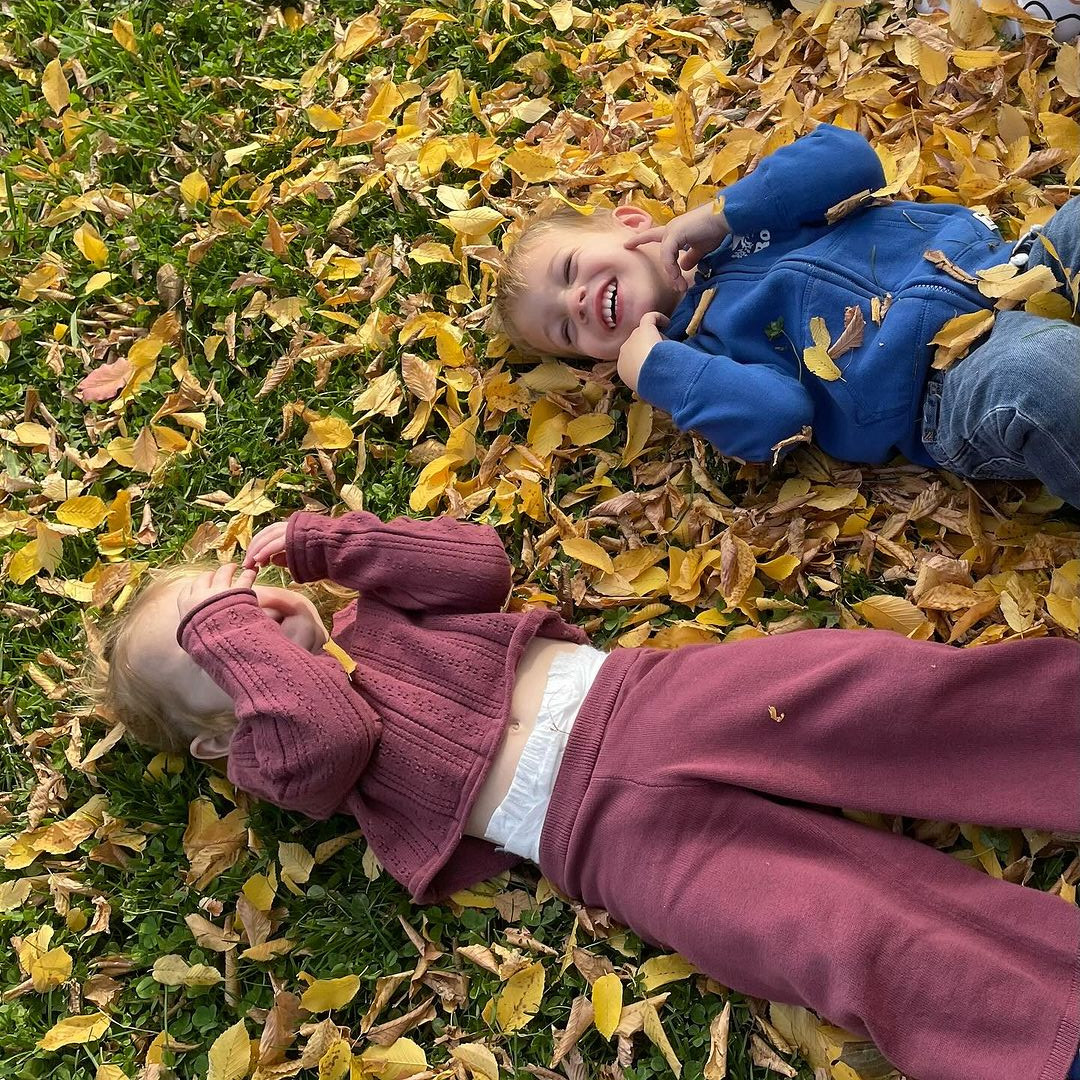 Two children lying on grass covered with yellow leaves