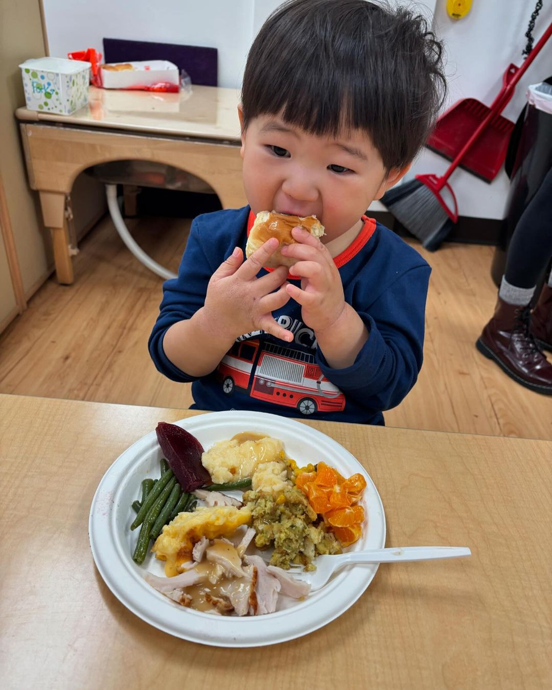 Child eating a roll with a plate of food on a table