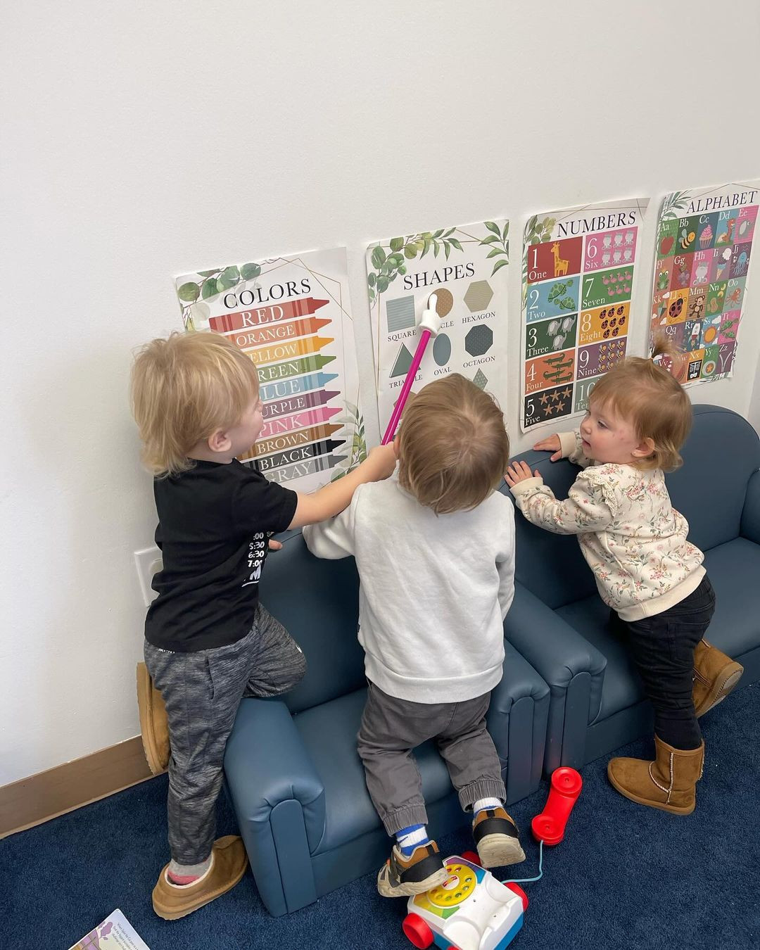 Three children standing on chairs looking at educational posters