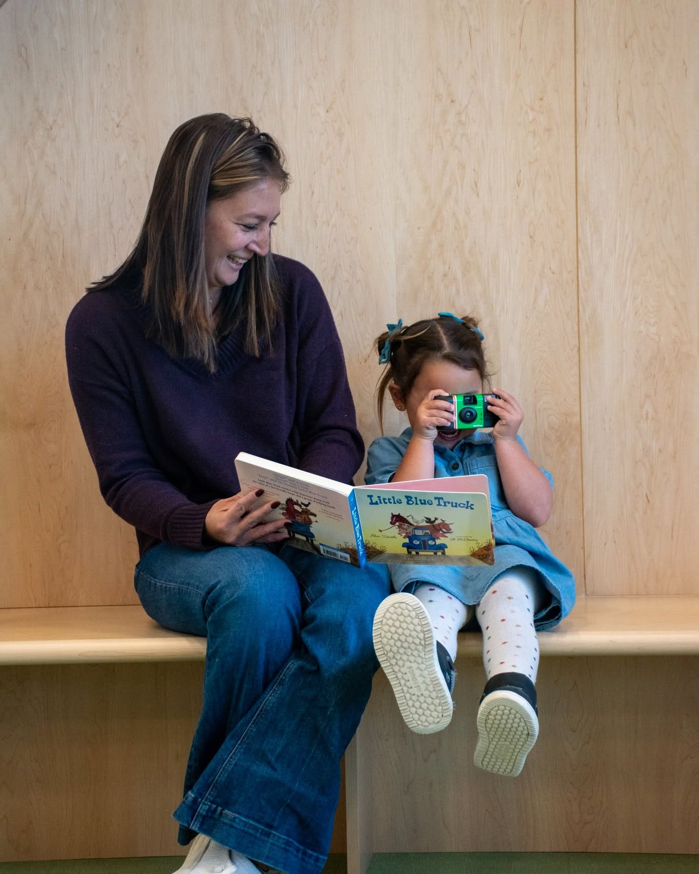 Adult and child reading Little Blue Truck book while child holds a toy camera