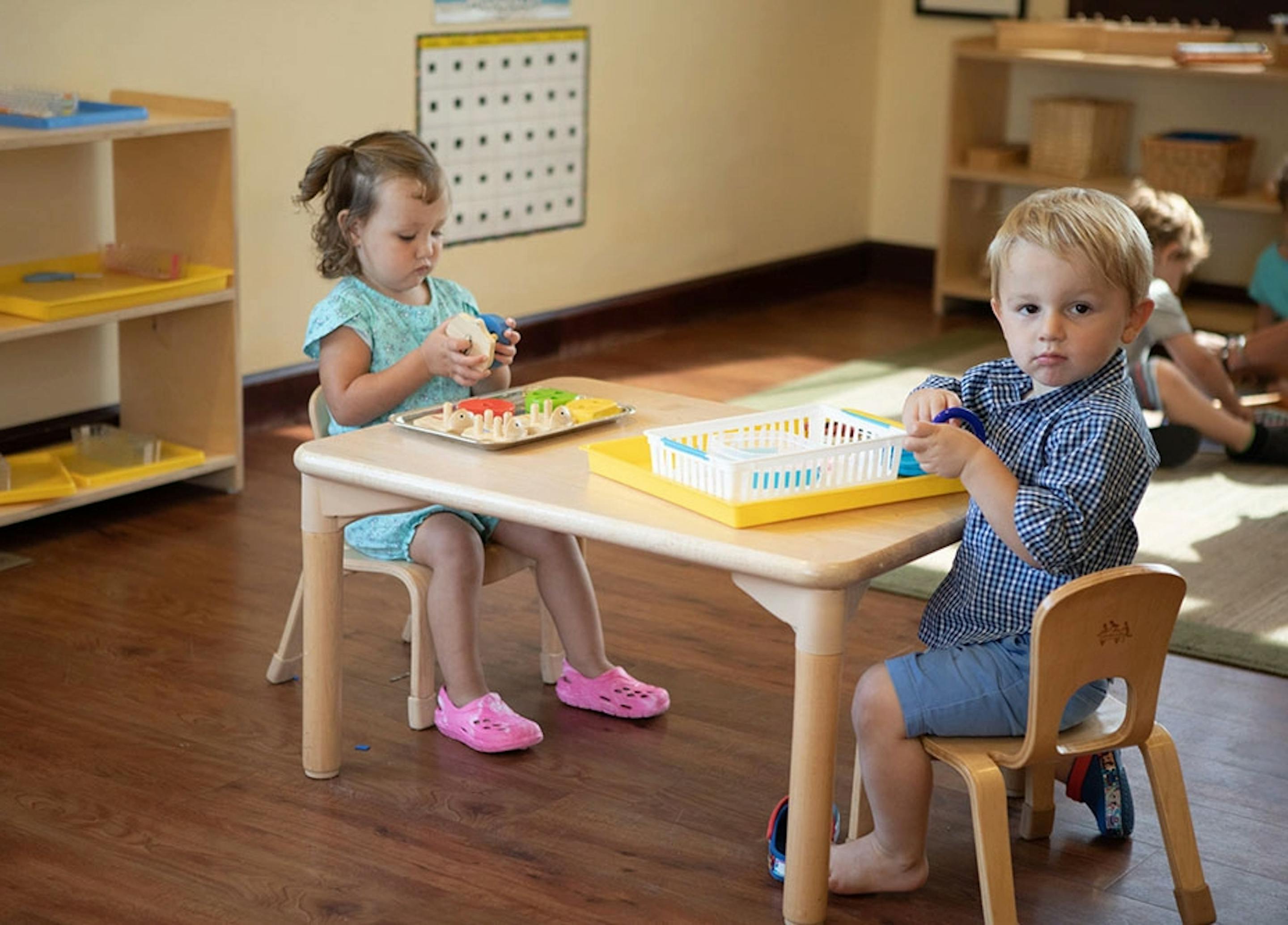 Two children sitting at a small table in a classroom
