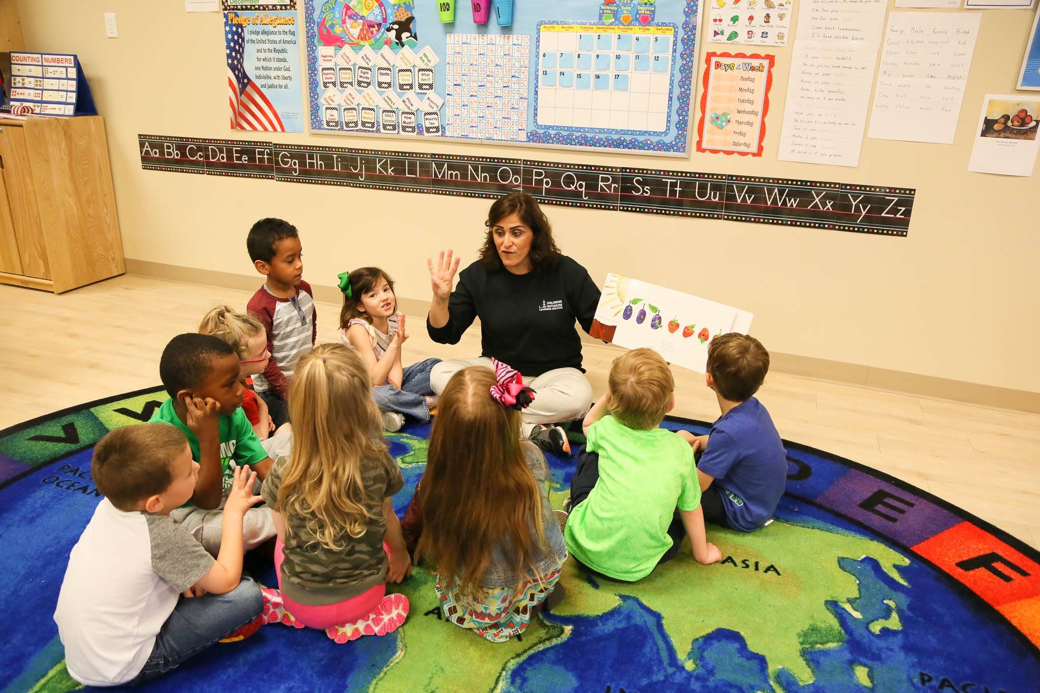 Teacher reading a book to a group of children sitting on a classroom rug