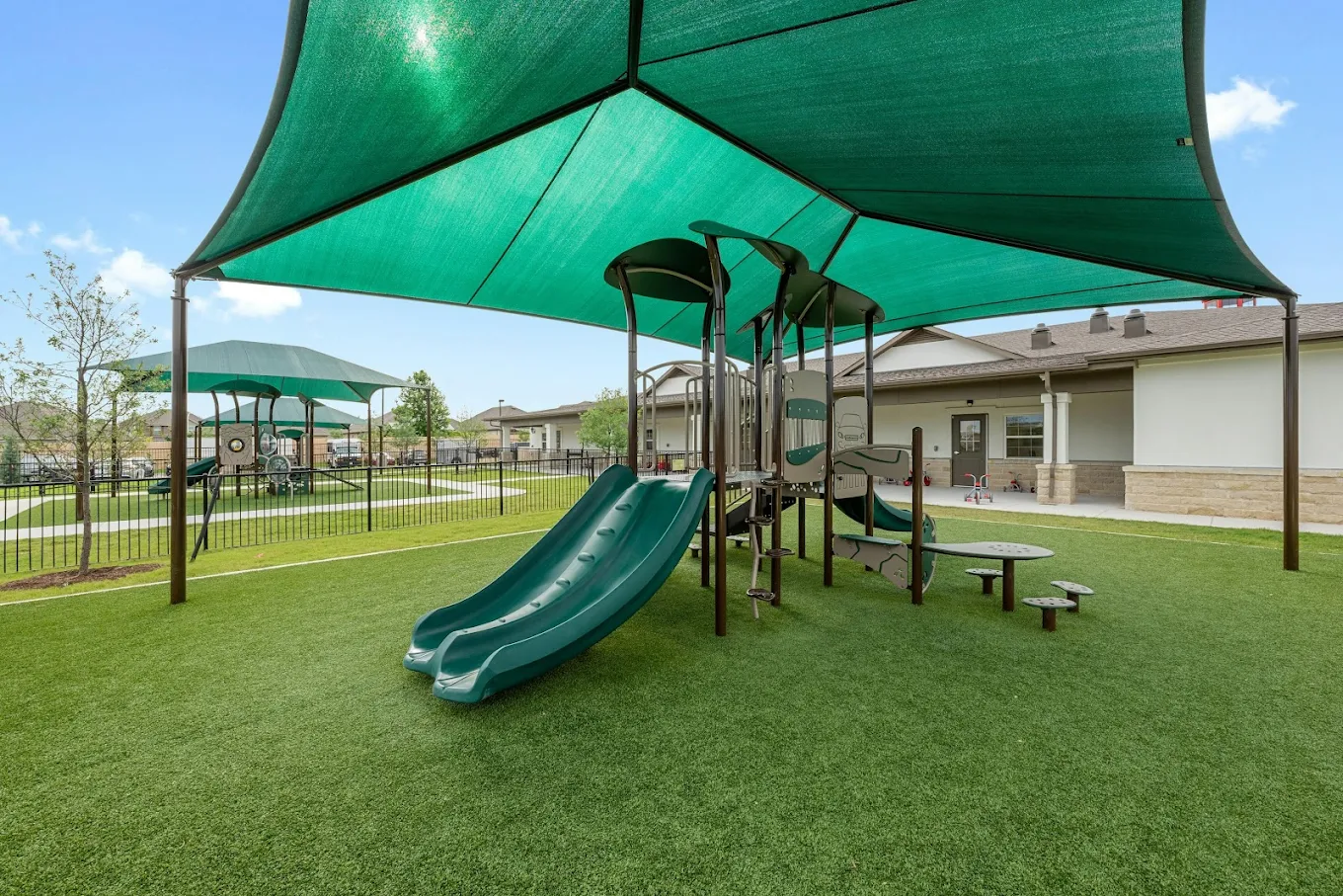 Playground equipment with a green shade canopy on an artificial grass surface
