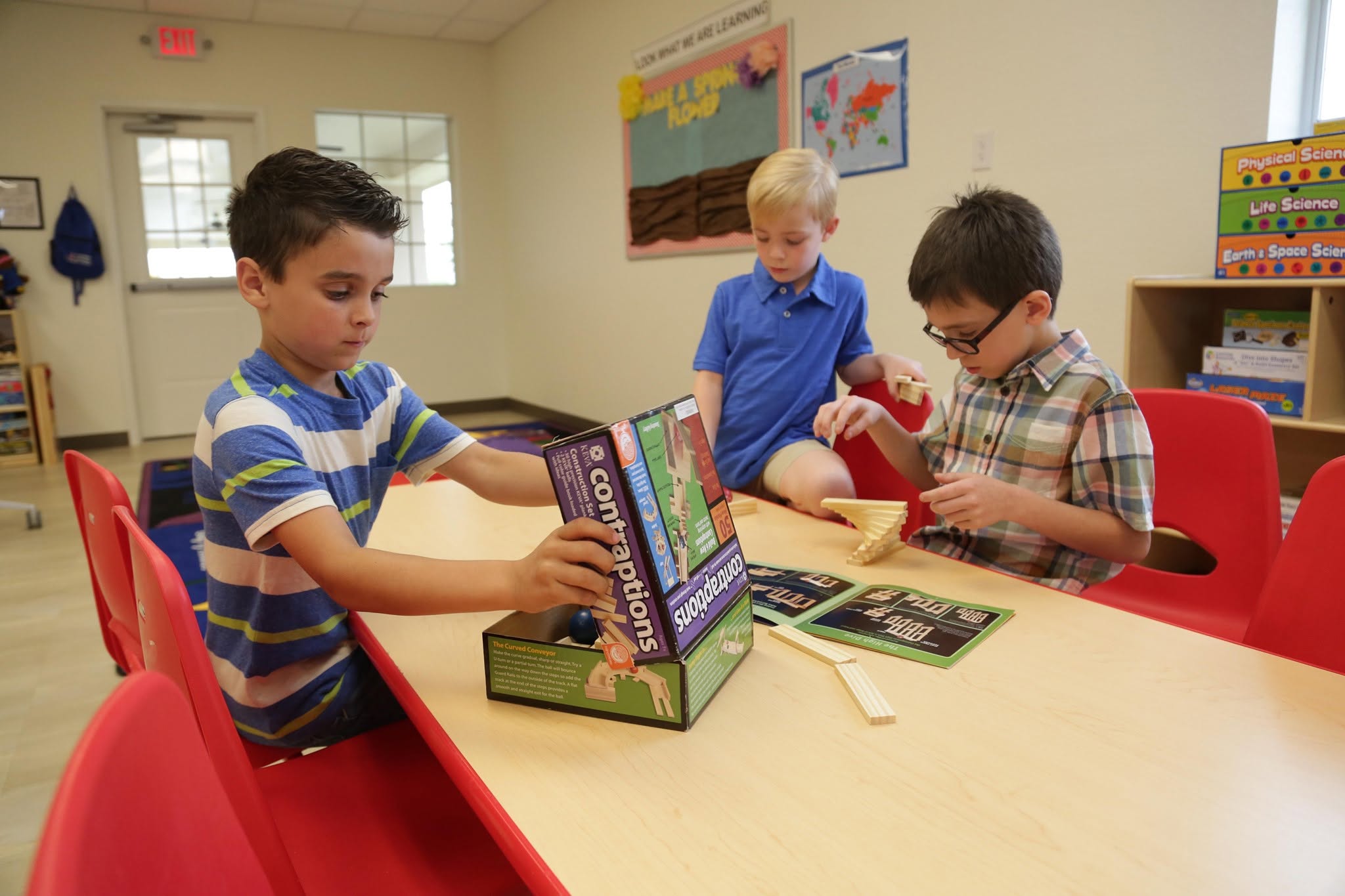 Three children building a Keva Contraptions set at a classroom table
