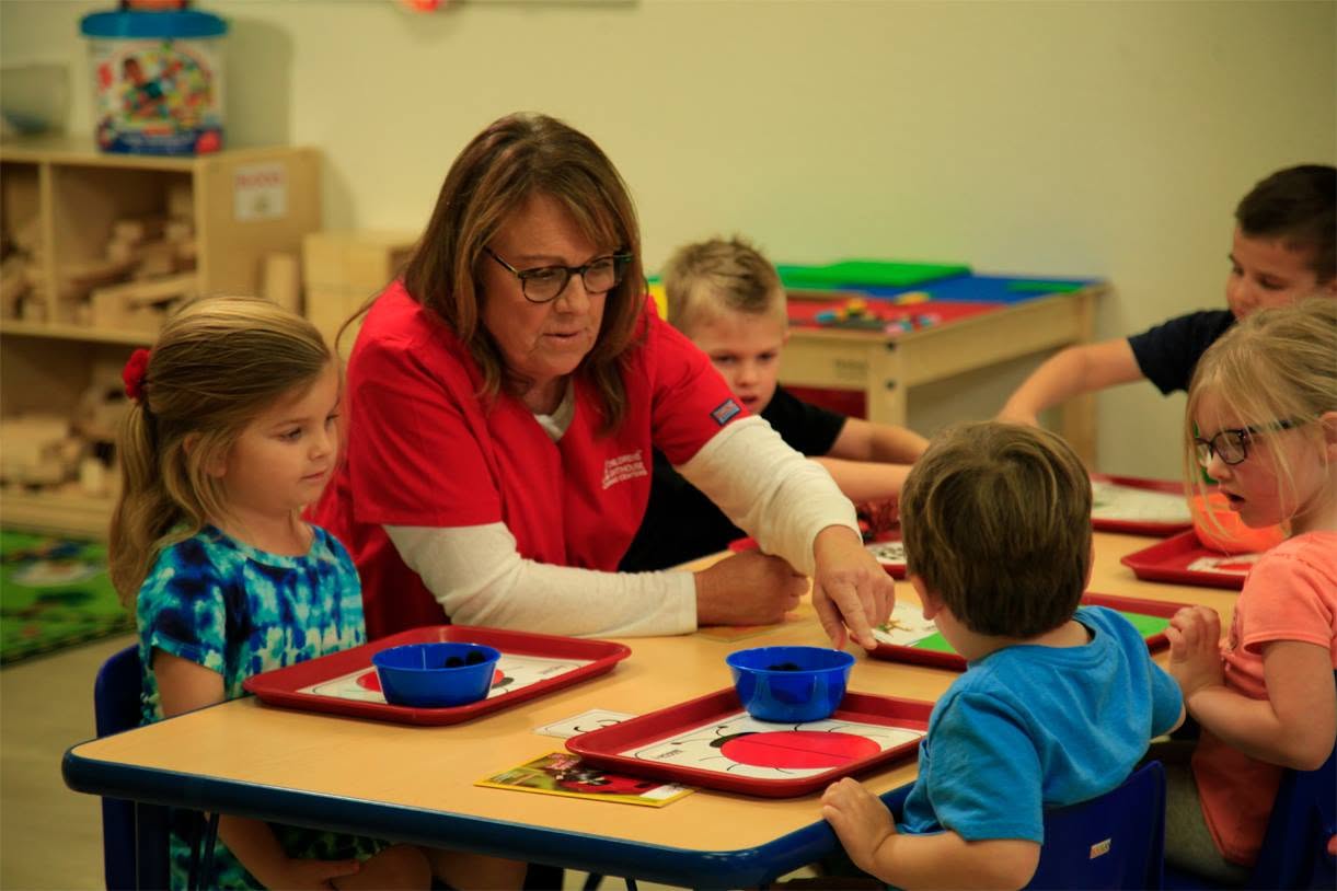 Adult supervising a group of children at a table with learning activities