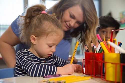 Adult and child drawing with colored pencils in a classroom