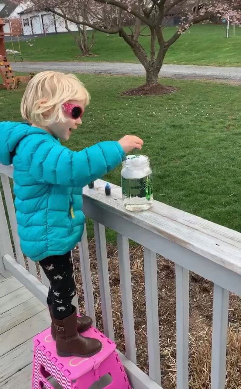 Child on a step stool reaching for a jar on a railing