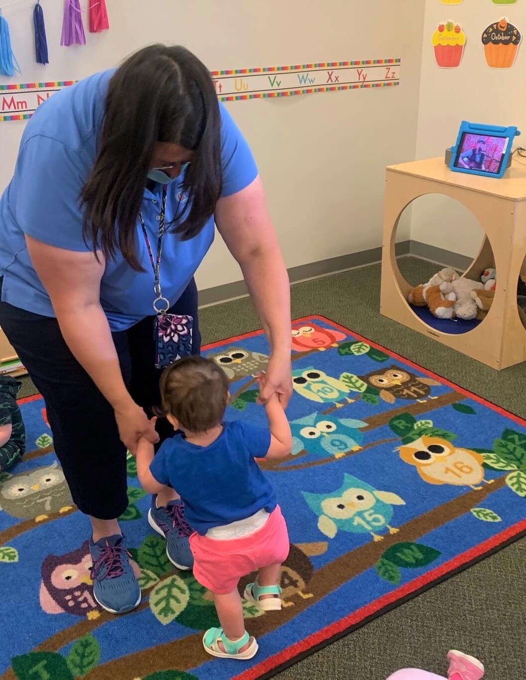 Person helping a child walk on an owl-patterned rug