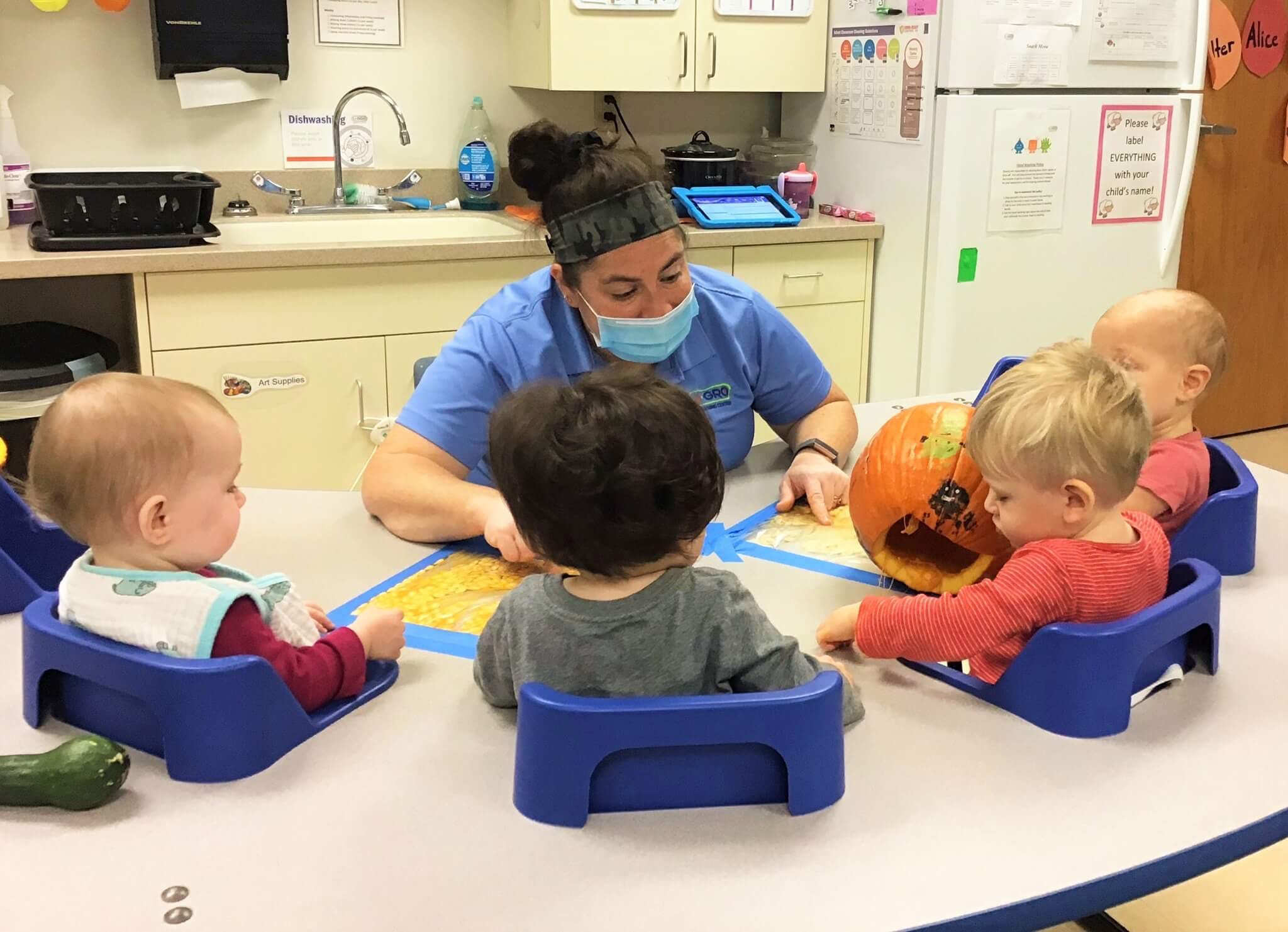 Adult and multiple children sitting at a table with a pumpkin