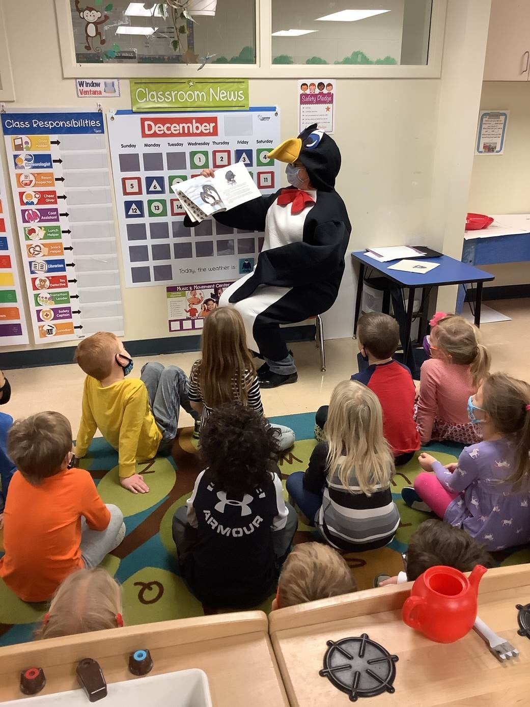 Person in a penguin costume reading a book to children in a classroom
