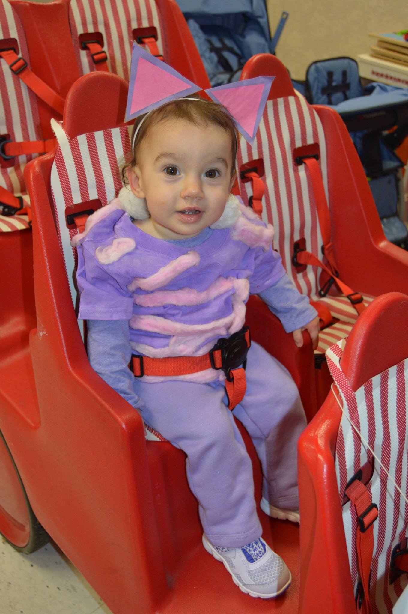 Child in a purple outfit and pink bow headband sitting in a red seat