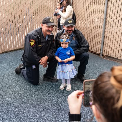 Two people in uniform kneeling next to a child, person taking photo in foreground