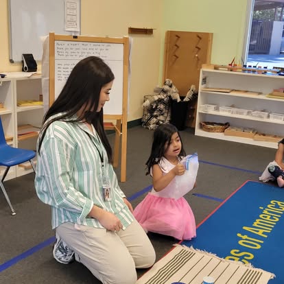 Person kneeling next to a child holding a white object in a classroom