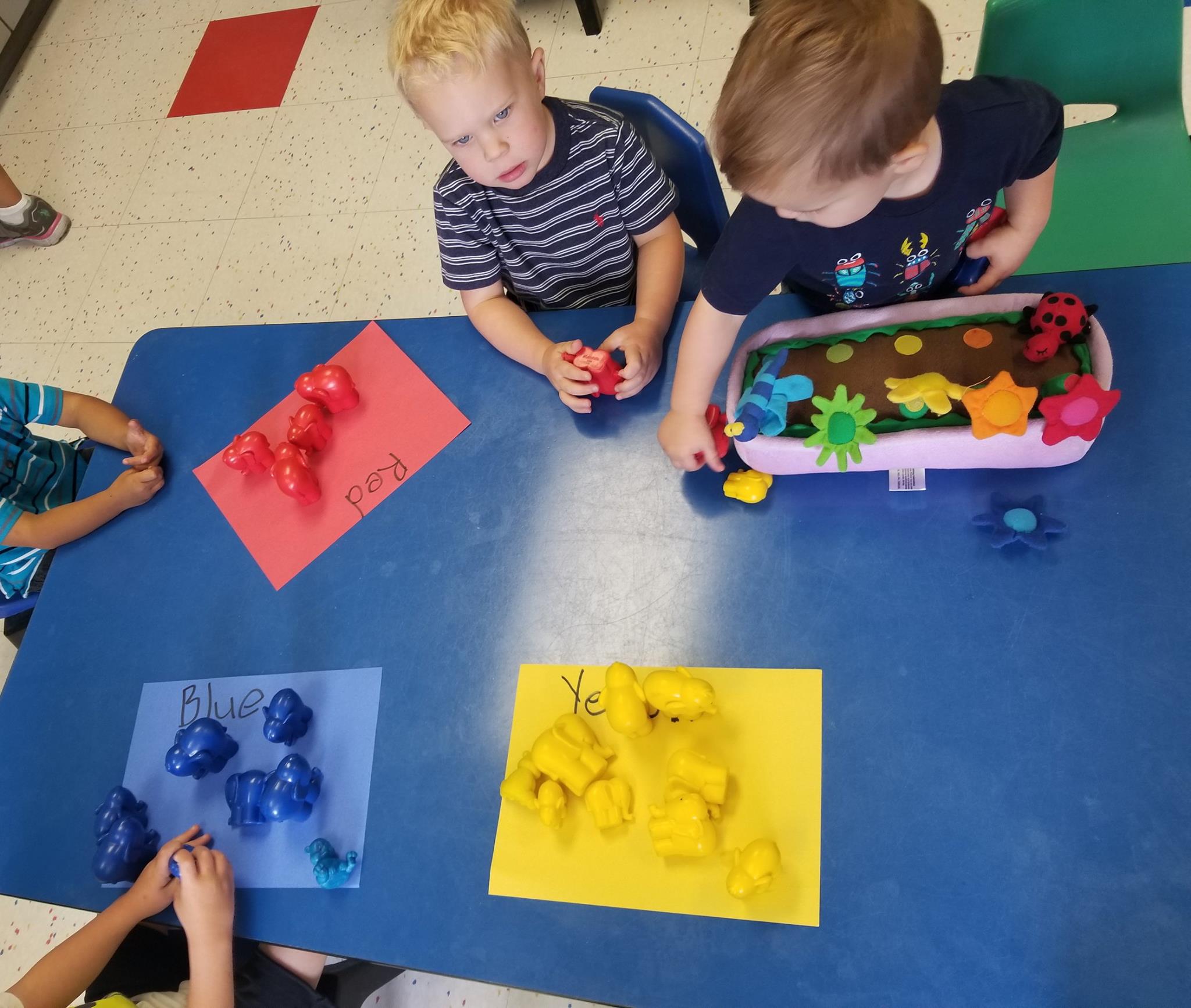 Children playing with colorful objects on a blue table