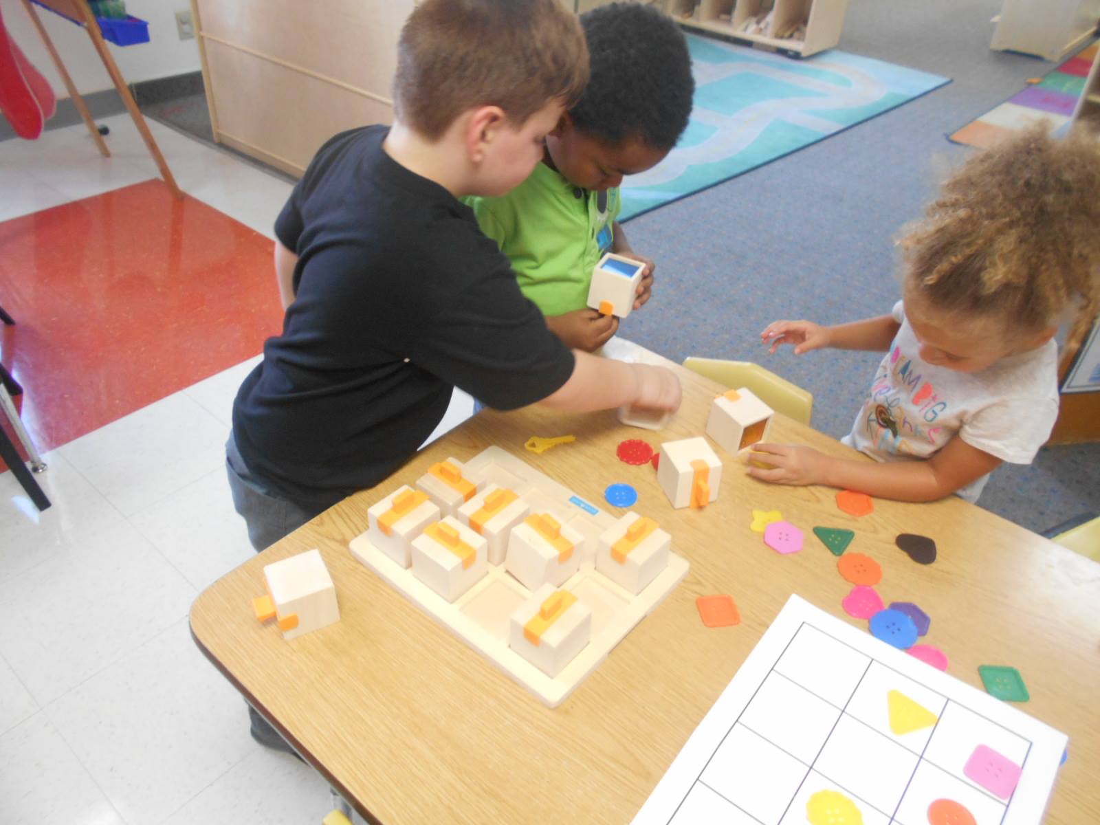 Three children playing with blocks and colorful shapes at a table