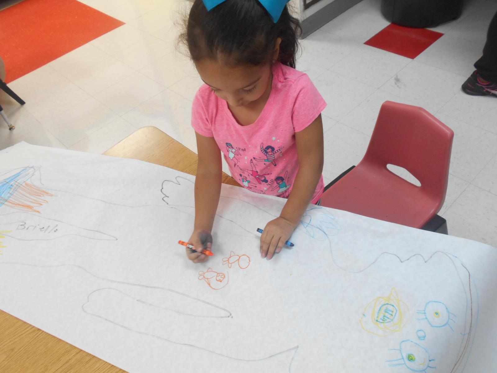 Child drawing on a large sheet of paper with crayons