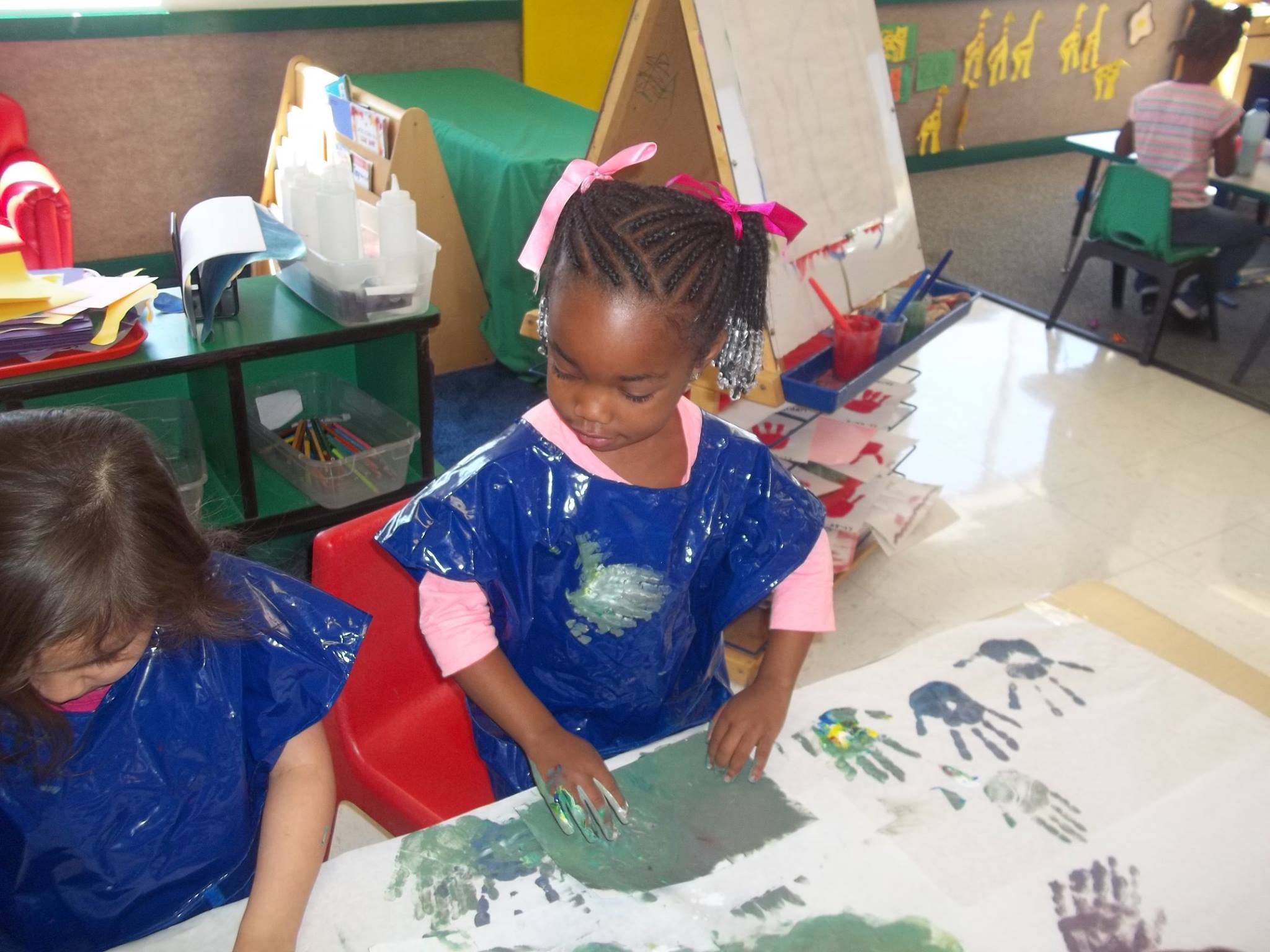 Child in smock making handprints on paper