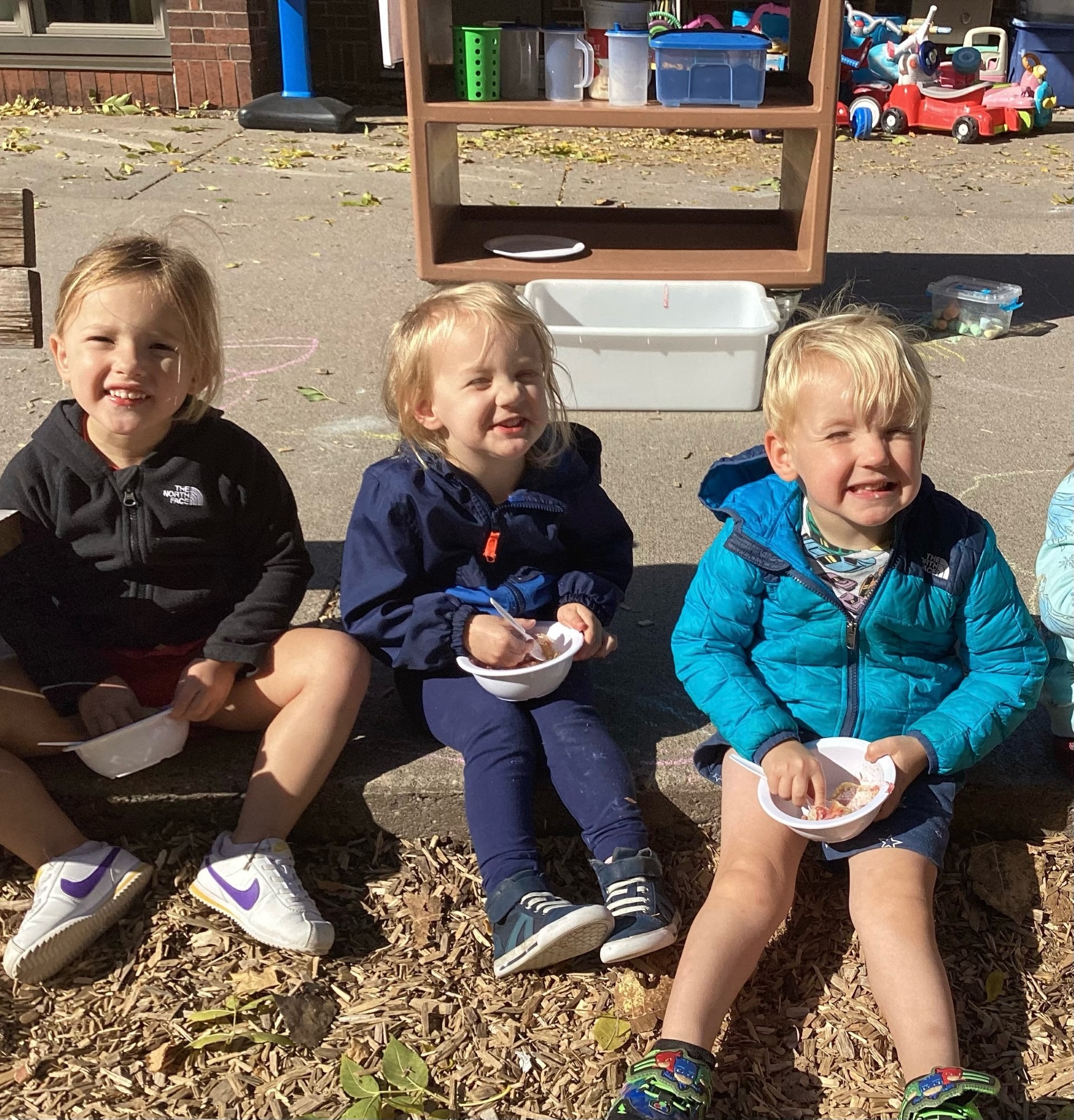 Three children sitting outdoors with bowls