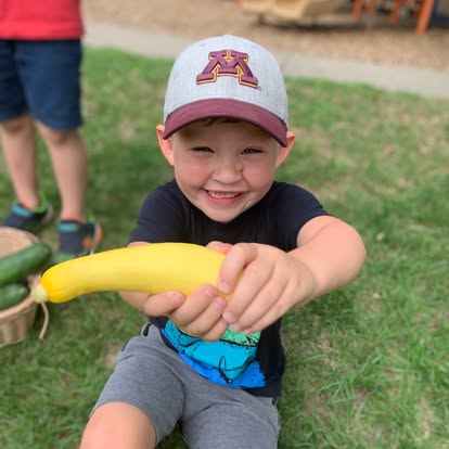 Child in a hat holding a yellow squash