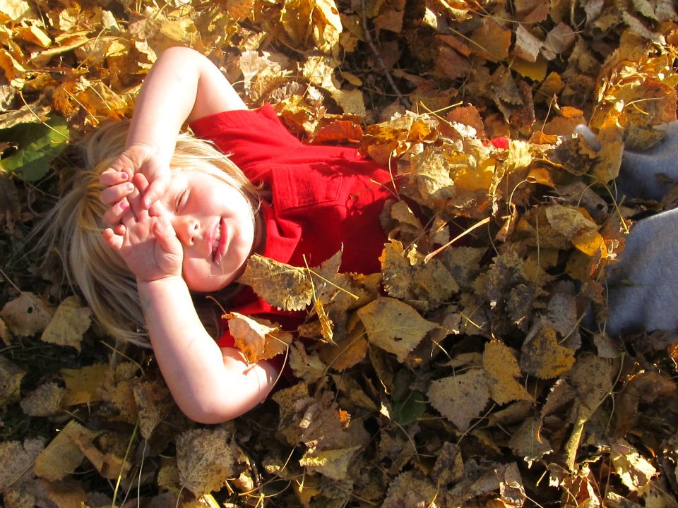 Child in a red shirt lying in a pile of autumn leaves