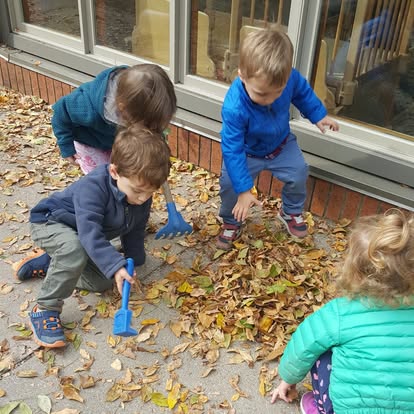 Children playing with leaves and small rakes outdoors