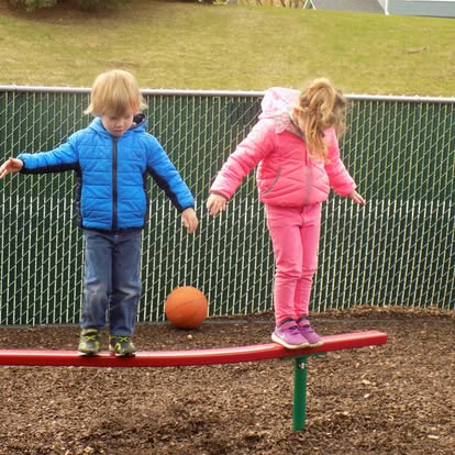 Two children balancing on a red beam on a playground