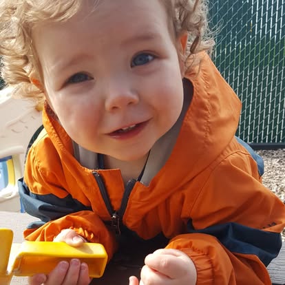Child in orange jacket holding a yellow toy
