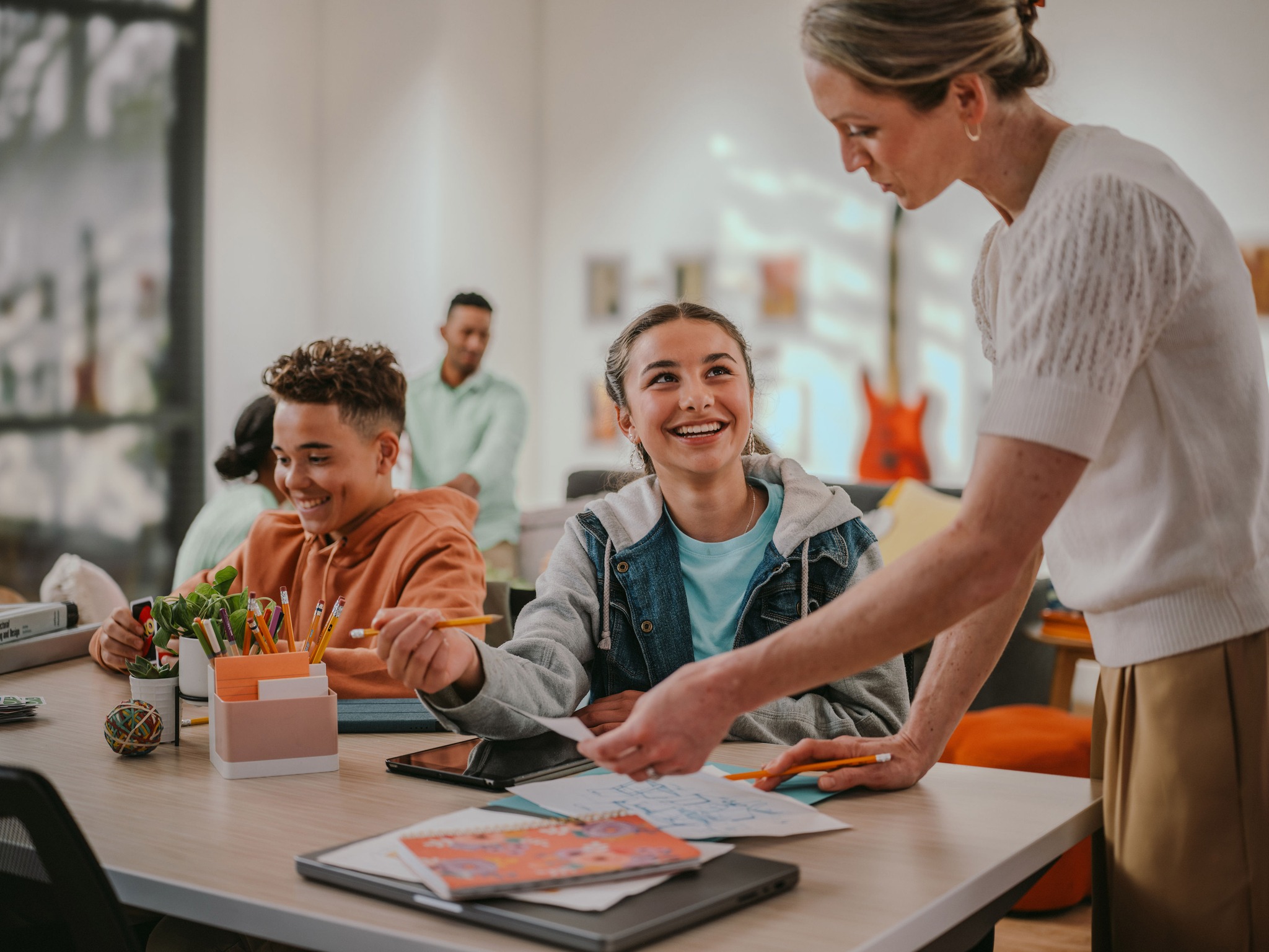 Adult handing paper to a teen at a table with another teen