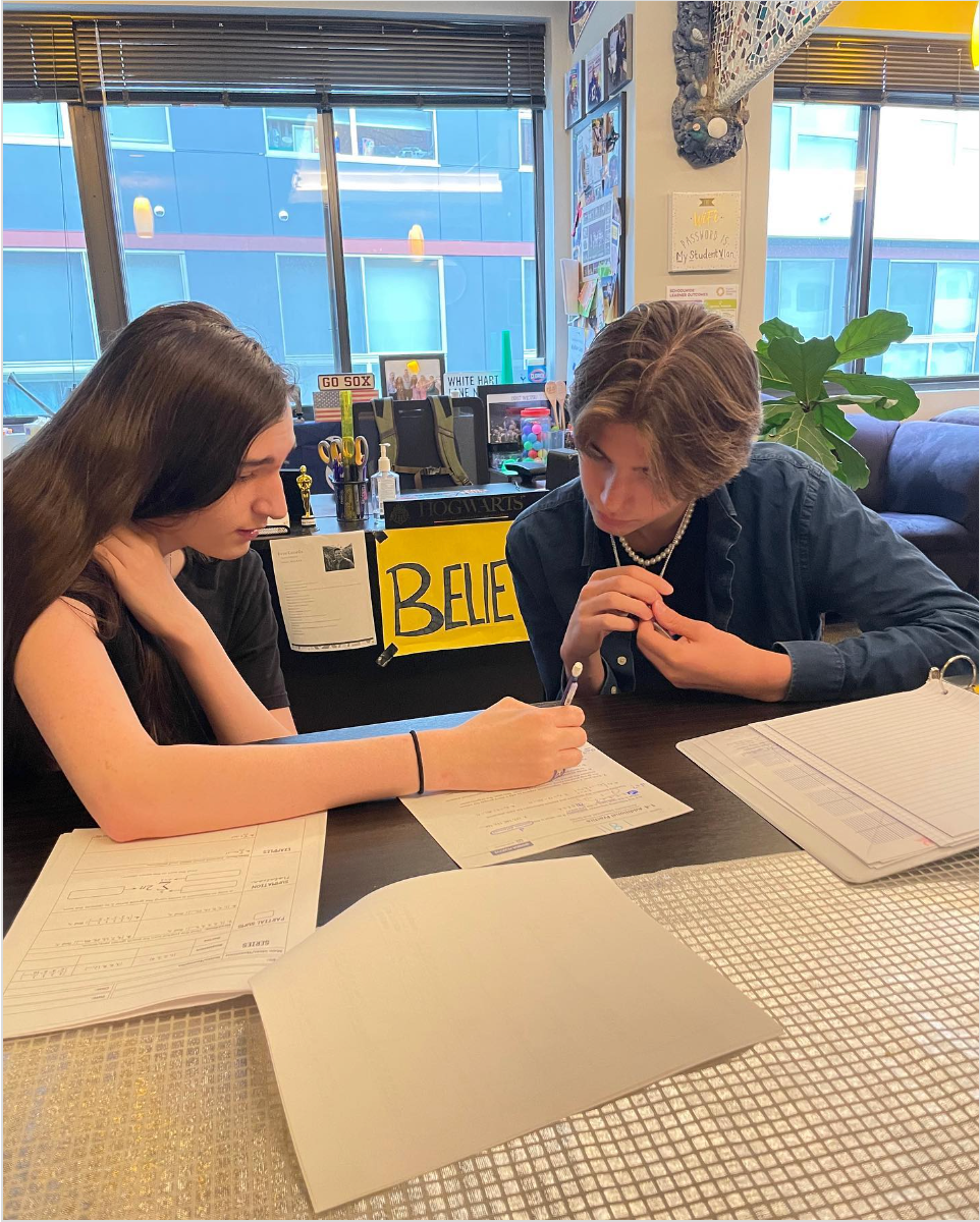 Two people sitting at a table with papers, one writing