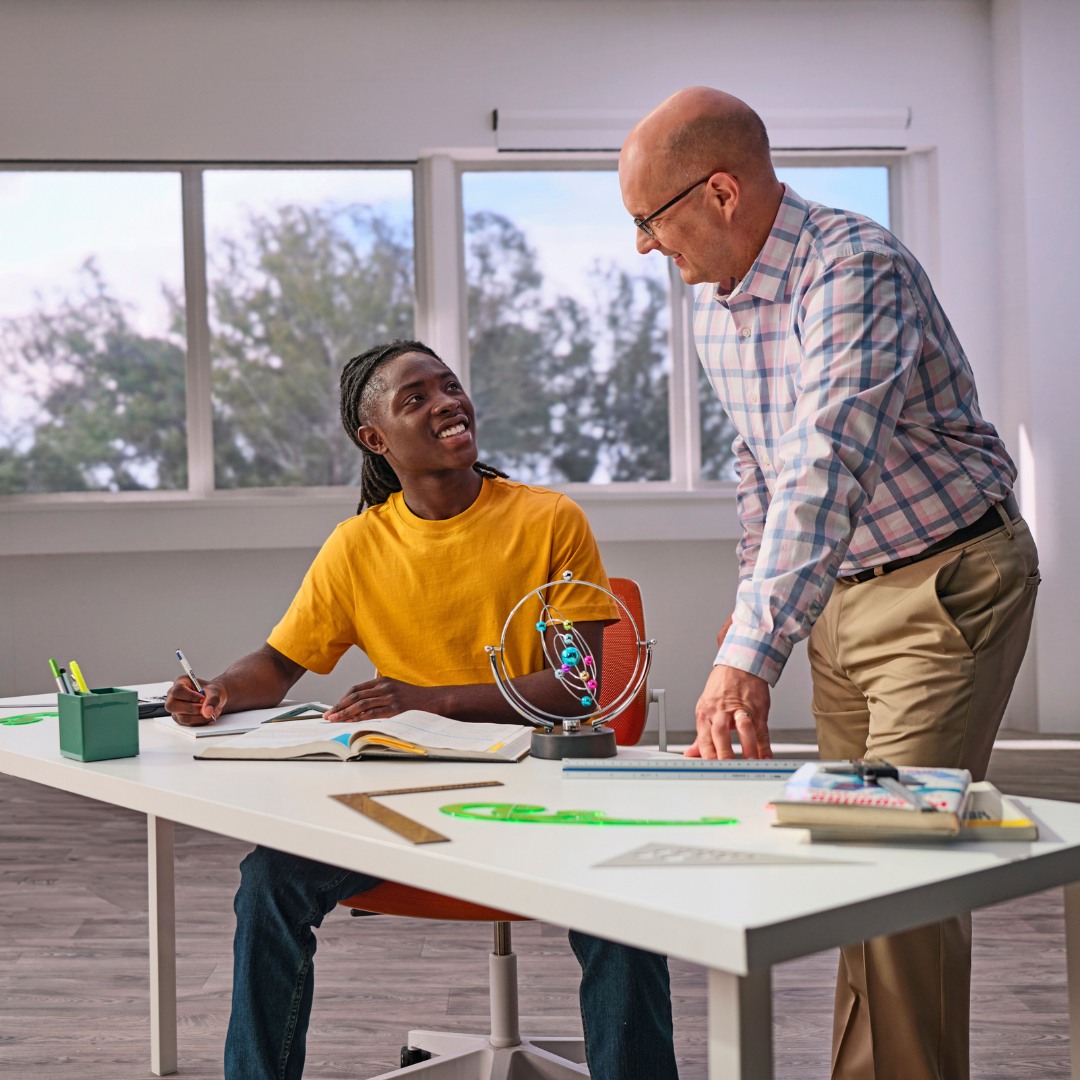 Adult and teen looking at each other across a desk with school supplies