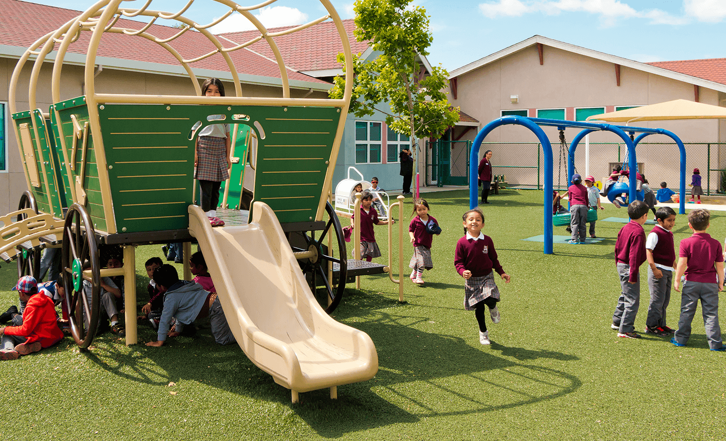 Children playing on a playground with a wagon-shaped play structure and slide