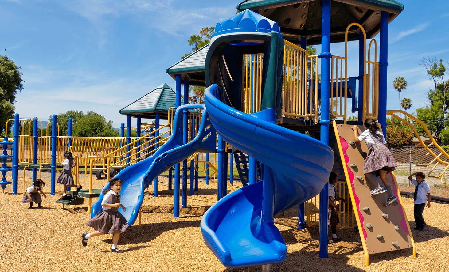 Children playing on a playground structure with slides and climbing wall