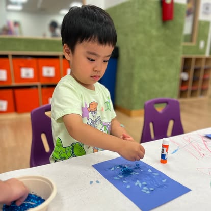 Child doing a craft with blue paper and small blue pieces