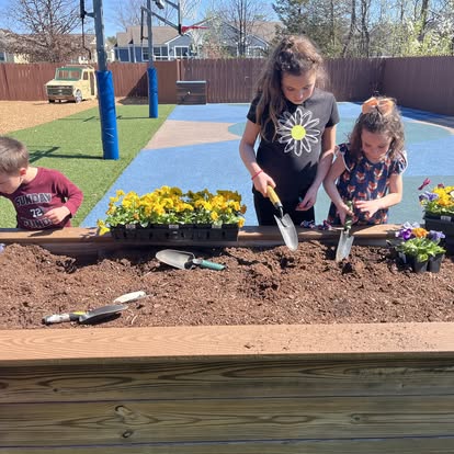 Two children and a teen planting flowers in a raised garden bed