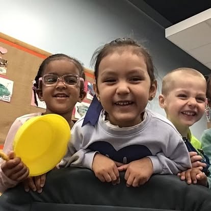 Three children smiling, one holding a yellow object