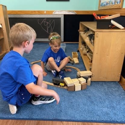 Two children playing with a toy train set on a blue rug