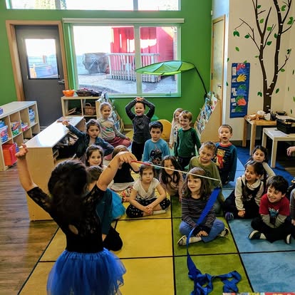Group of children sitting on a colorful floor watching someone dance with a ribbon