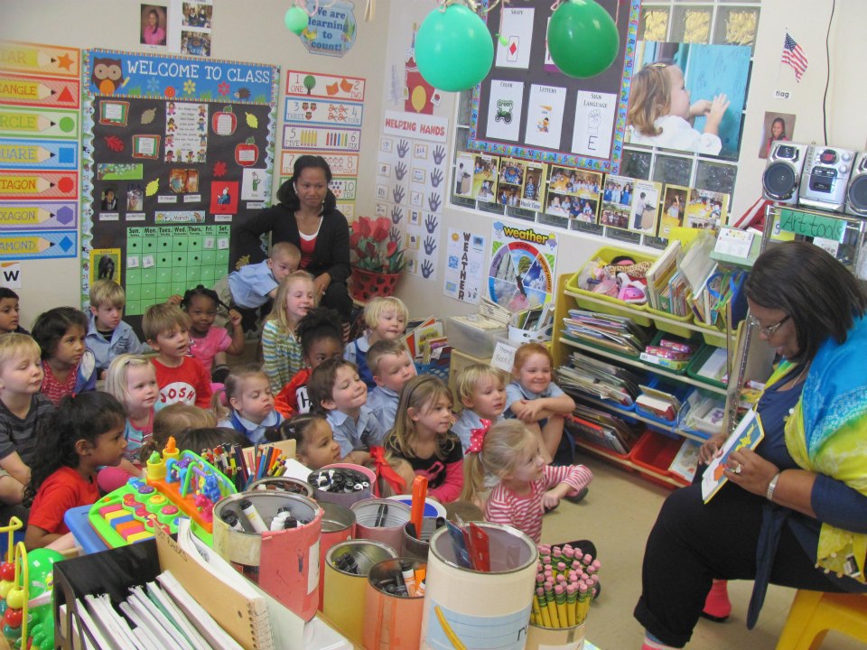 adult reading a book to a group of young children sitting on the floor in a classroom