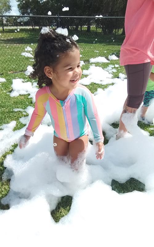 Child in a colorful swimsuit standing in white foam on grass