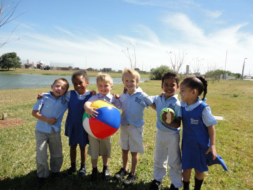 Six children in school uniforms standing outdoors with a beach ball
