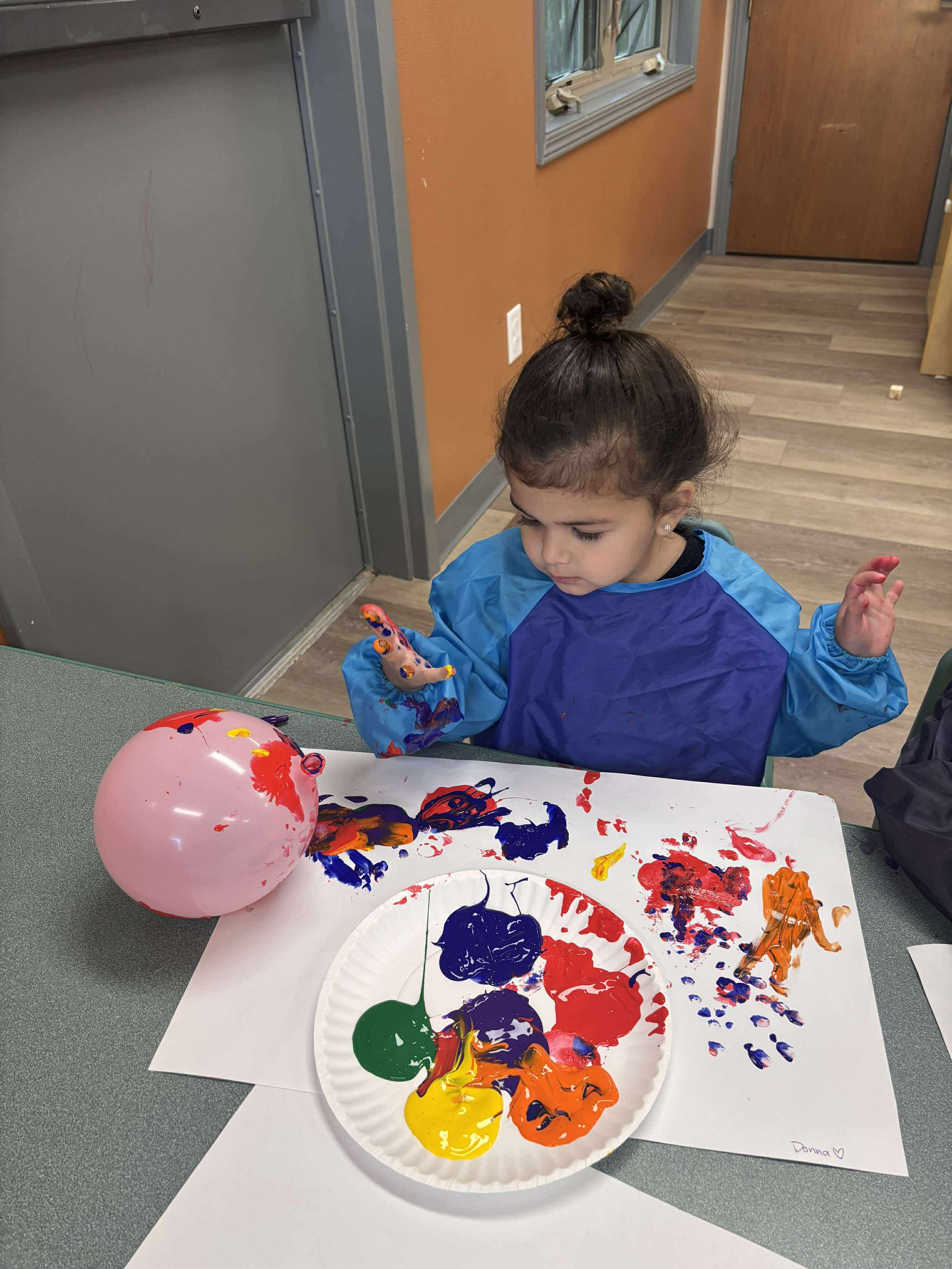 Child in a smock finger painting with multiple colors on paper