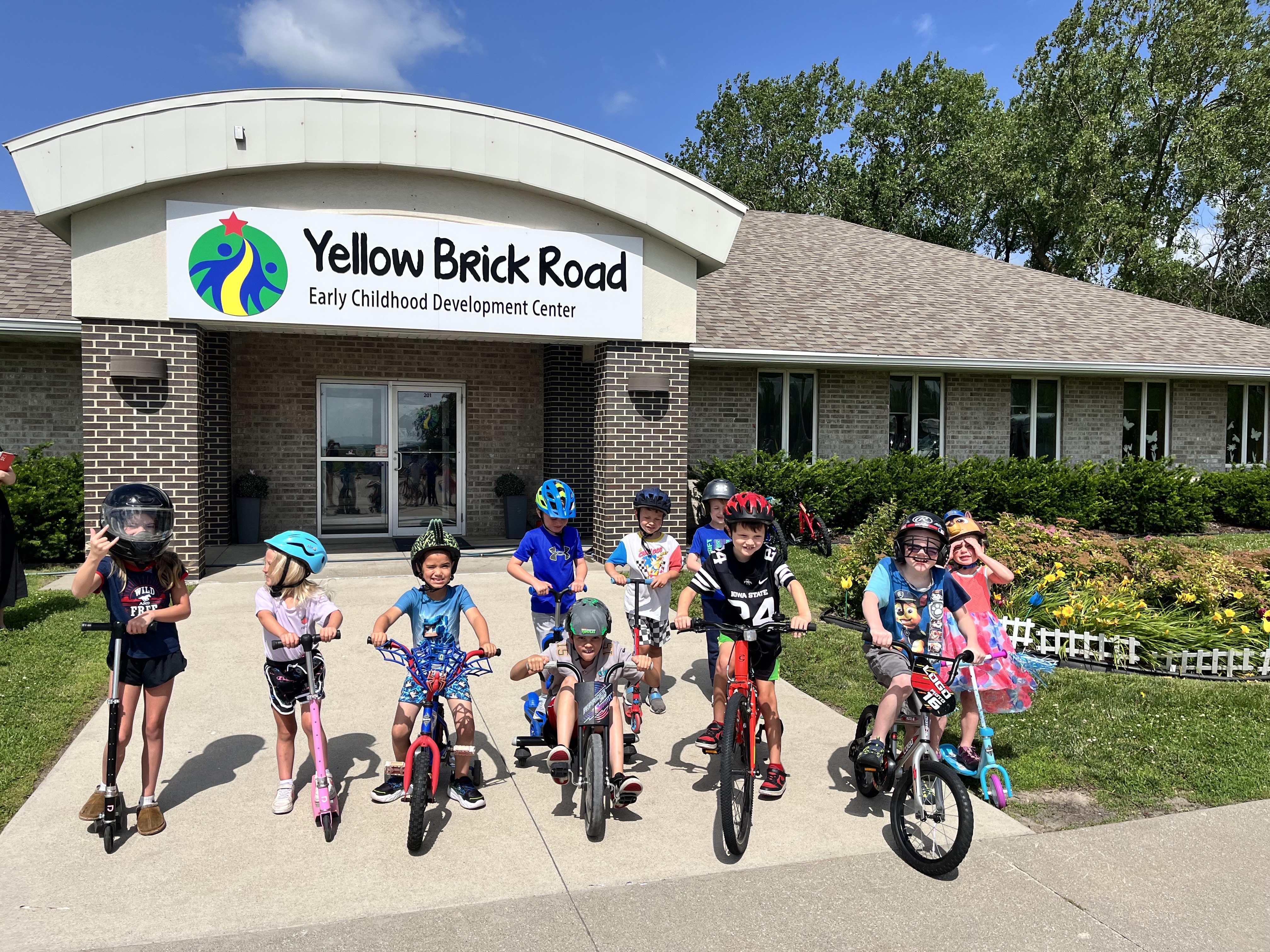 Children on bikes and scooters in front of Yellow Brick Road Early Childhood Development Center