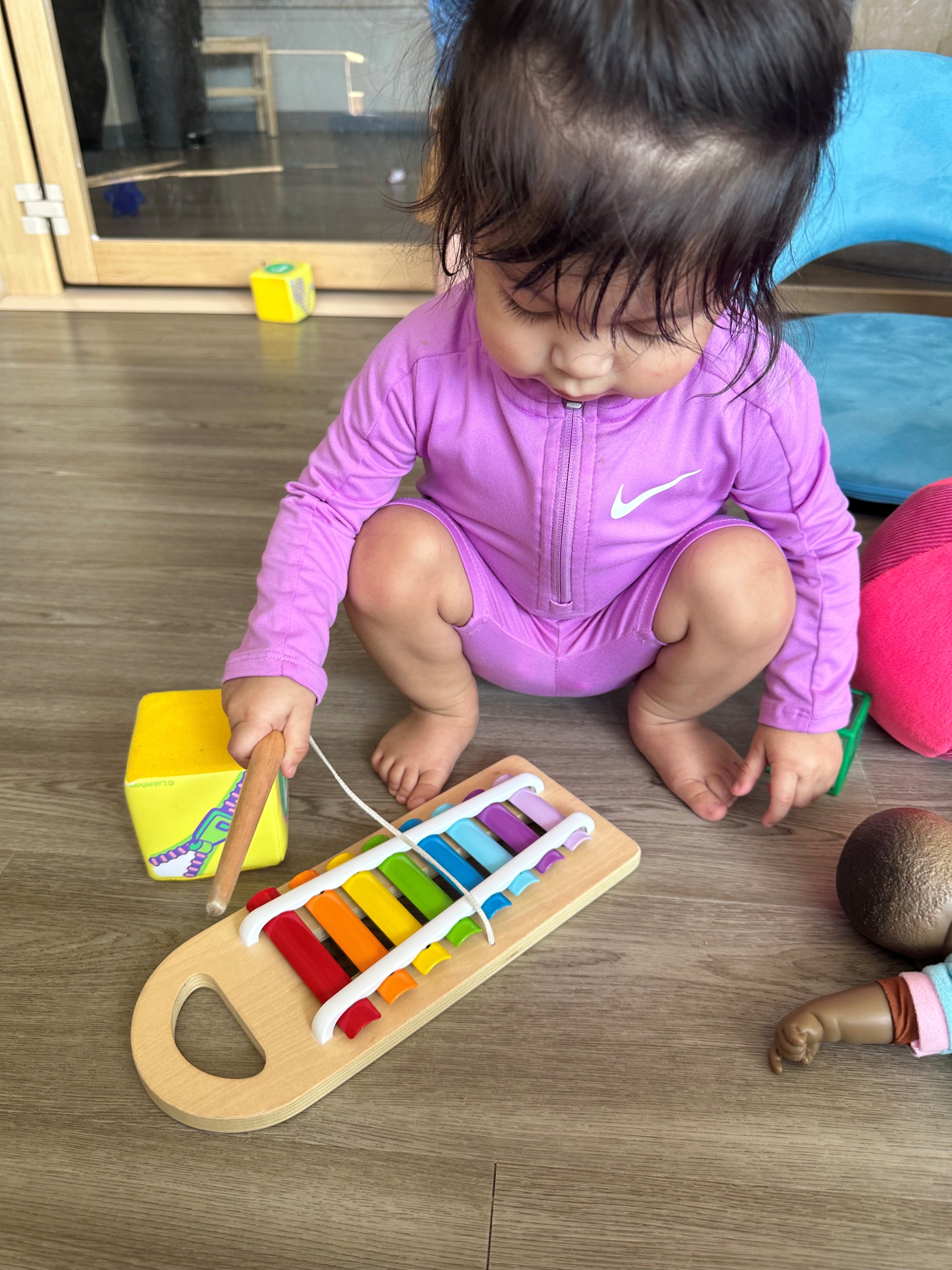 Child crouching on the floor, playing a colorful toy xylophone