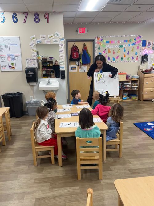 Teacher holding up a letter 'P' for children seated at a table in a classroom
