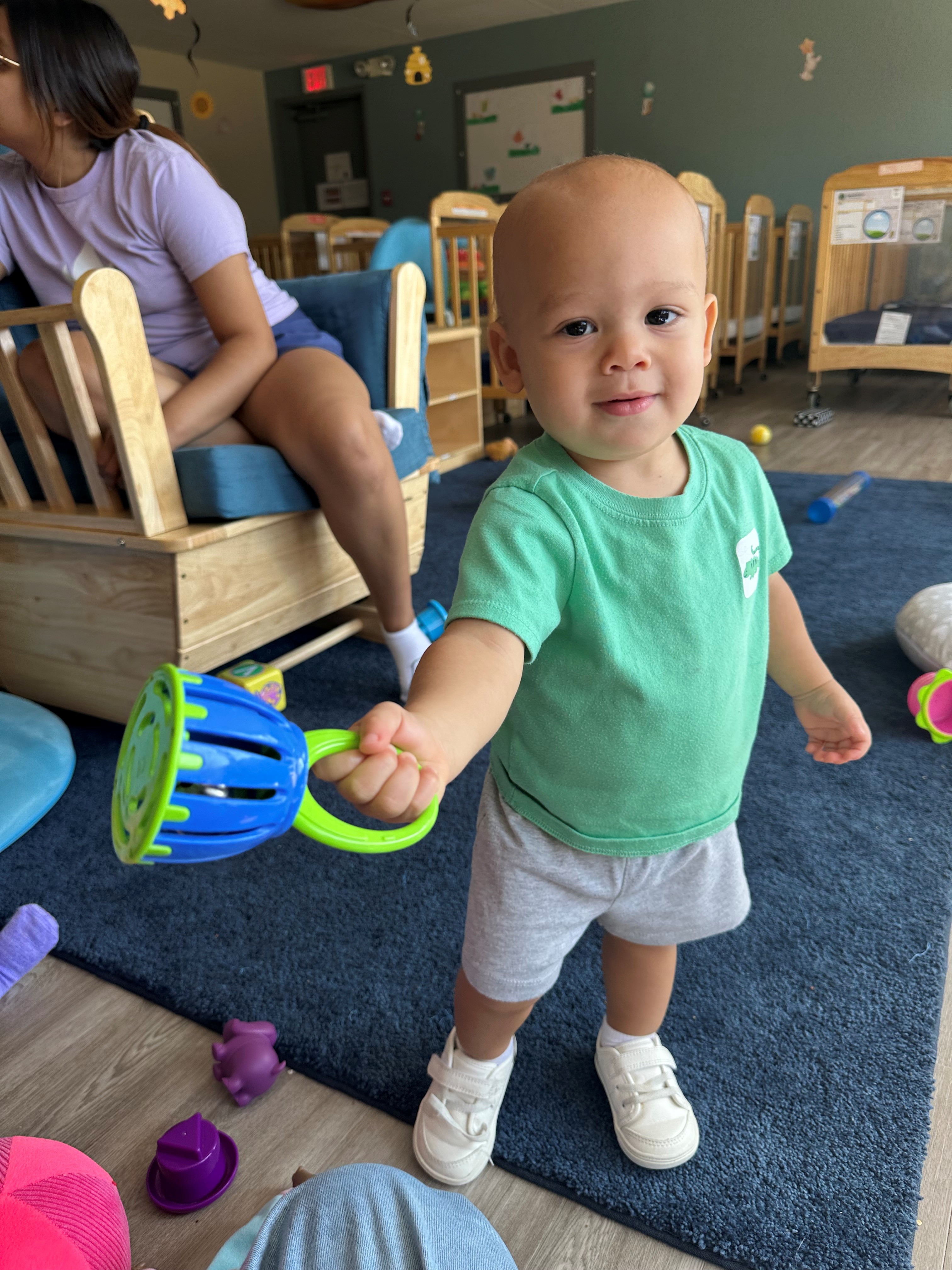 Child in a green shirt holding a rattle in a classroom
