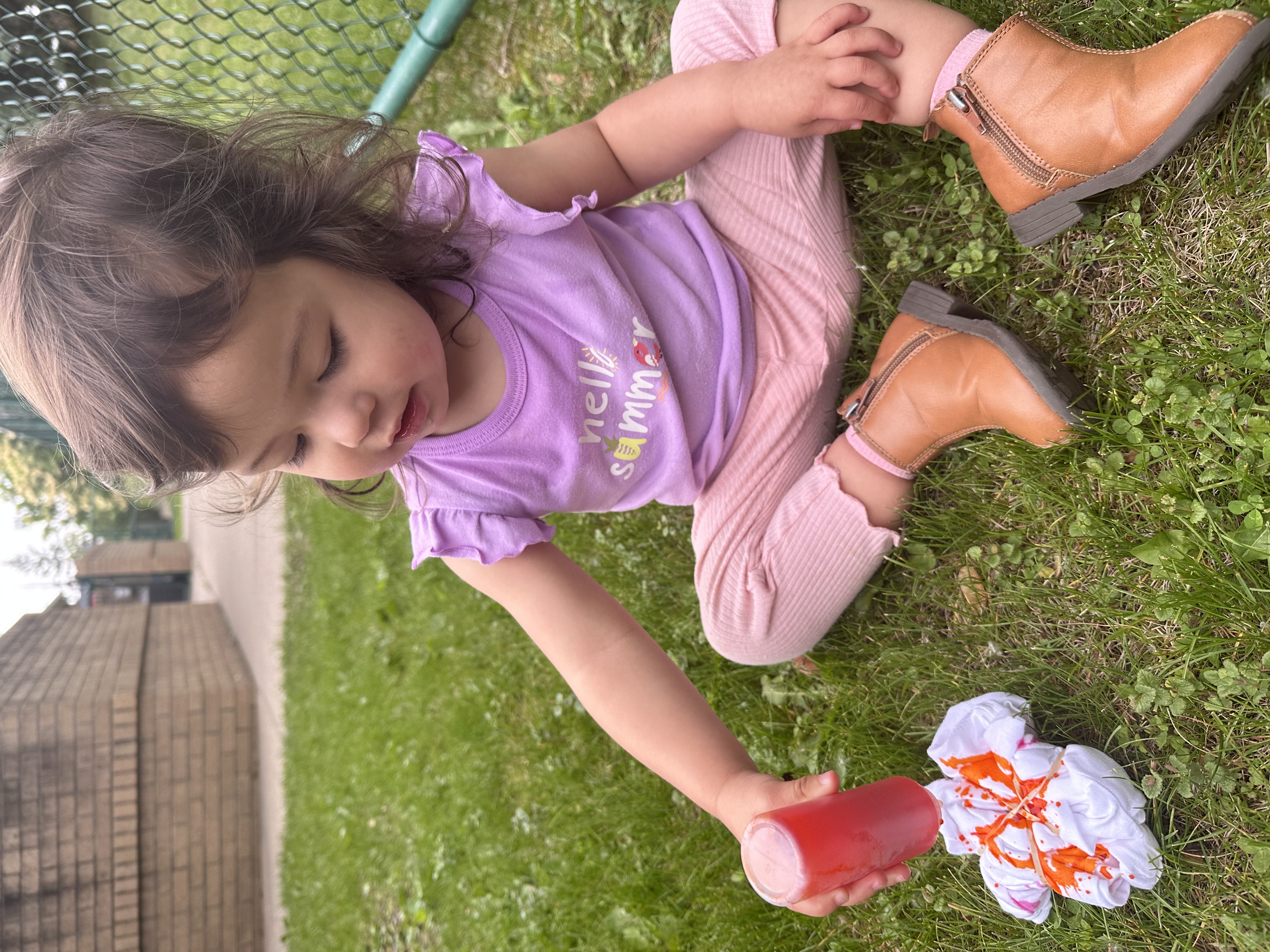 Child sitting on grass applying dye to a folded white t-shirt
