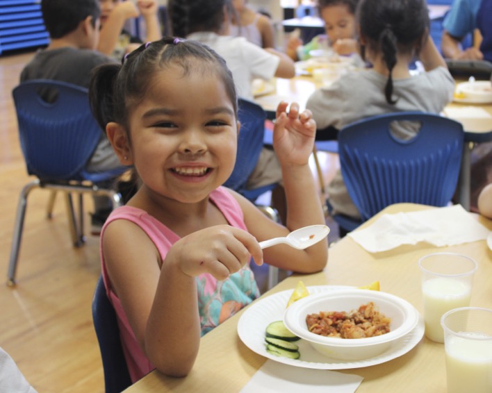 Child at a table with a bowl of food and a spoon