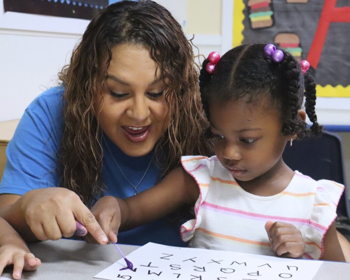 Adult and child learning letters on paper in a classroom