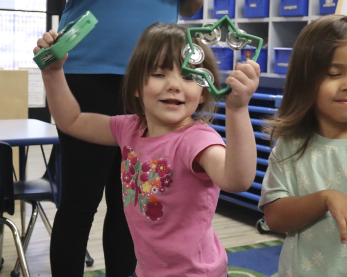 Child playing two musical instruments in a classroom